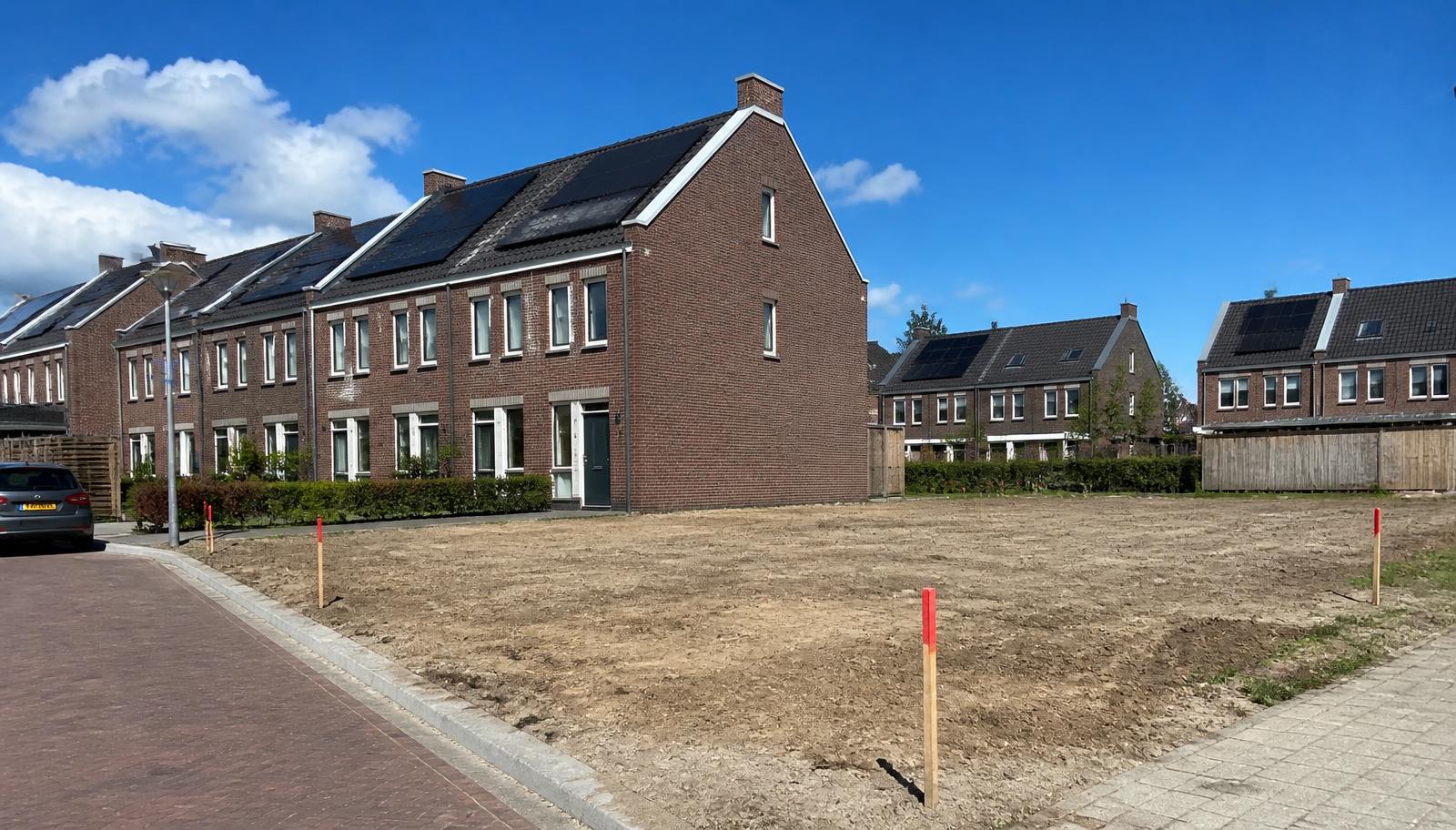 Afgebouwde woningen naast een onbebouwde bouwkavel met piketpaaltjes