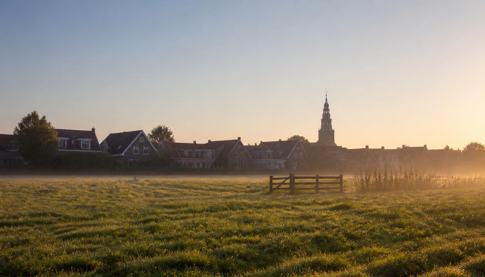 Onbebouwd weiland aan de dorpsrand met woningen op de achtergrond